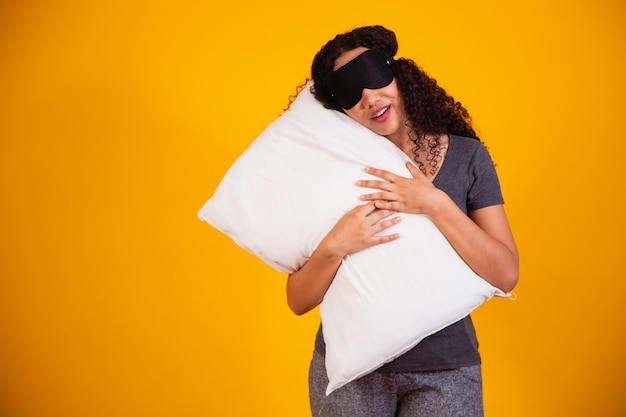 Фотография афро девушки обнимая подушку на желтом фоне. Крупным планом молодая девушка держит подушку в руках. концепция сна