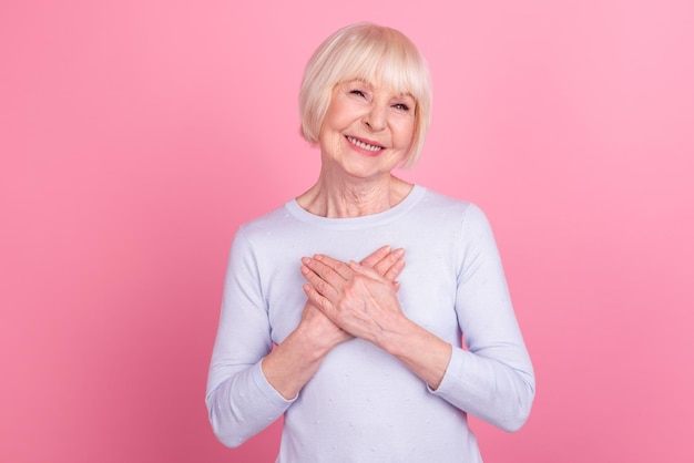 Photo of aged cheerful lady arms on chest sincere enjoy grateful honest promise isolated over pink color background