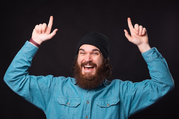 Foto di stupito uomo barbuto in camicia blu rivolta verso l'alto su sfondo nero