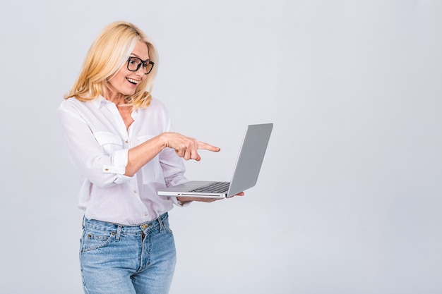 Photo of amazed shocked surprised senior mature old woman holding laptop computer isolated on white grey background.