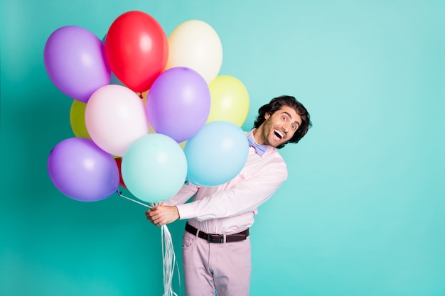 Photo of amazed young guy hold colorful hellium balloons isolated on turquoise color background