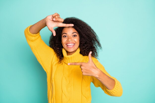 Photo of amazing dark skin lady making imaginary frame taking shot wear yellow knitted pullover isolated blue teal color wall