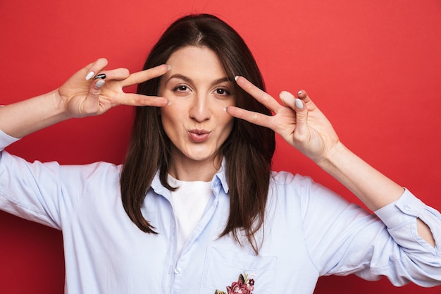 Photo of an amazing happy young beautiful woman posing isolated over red wall wall make peace gesture.