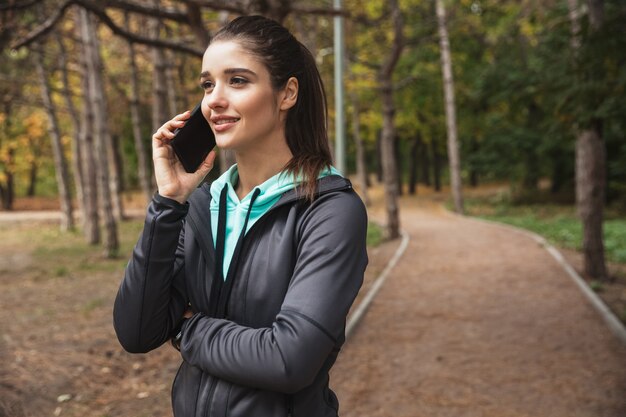 携帯電話で話している公園の屋外で驚くべき若いかなりフィットネスの女性の写真。