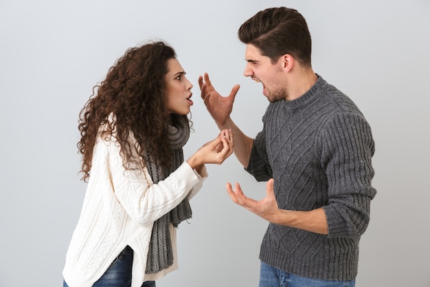 Foto foto di uomo arrabbiato e donna che urla a vicenda in piedi faccia a faccia, isolata sopra il muro grigio