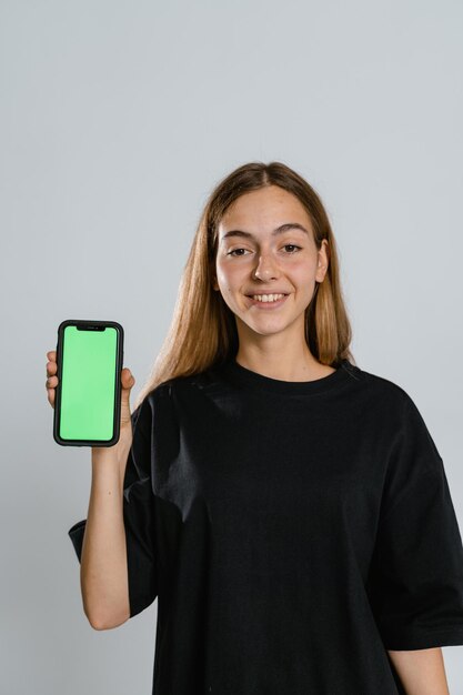 Photo app ad smiling pretty woman holding smartphone with white blank device screen in hand close up to camera gadget with empty free space for mockup banner isolated selective focus
