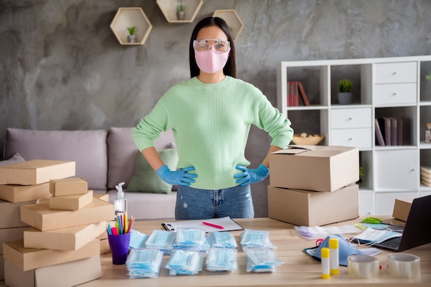 Photo of asian lady business organized orders facial flu cold masks global spread thousands satisfied customers preparing packs for delivering arms by sides confident home office indoors