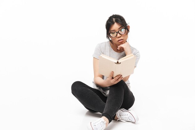 Photo of asian thoughtful beautiful young woman posing isolated over white wall   holding book reading.