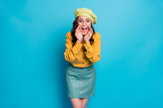 Photo of astonished crazy girl scream hand mouth share confidential incredible information wear yellow good look clothes headwear isolated over blue color background