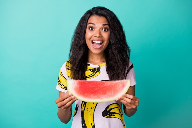 Photo of astonished dark skin girl hold delicious watermelon slice isolated on turquoise color background