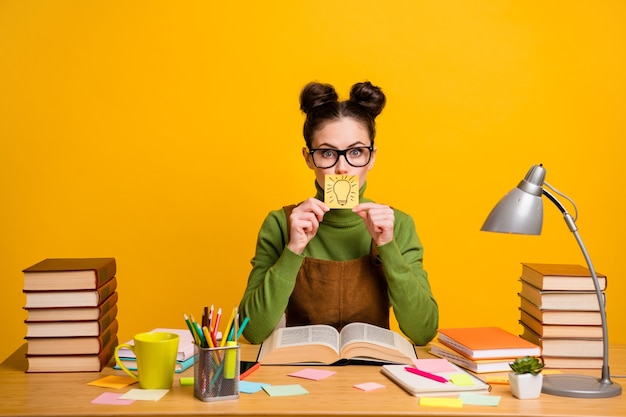 Photo of astonished high school girl sit table close paper sticker have incredible secret idea