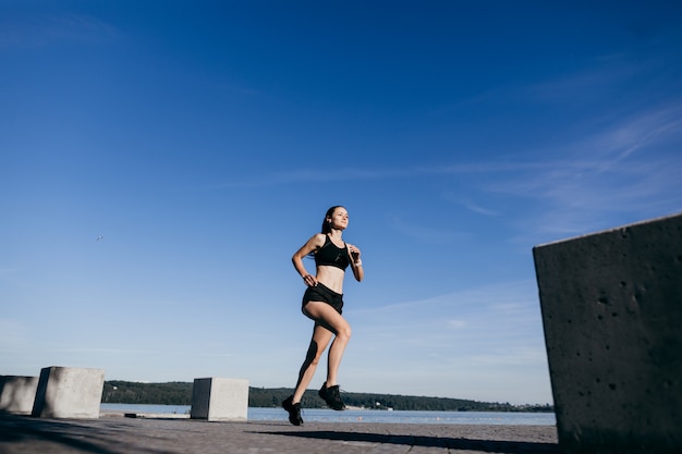 Foto di una ragazza atletica vestita di nero durante una corsa mattutina su una spiaggia della città al mattino.