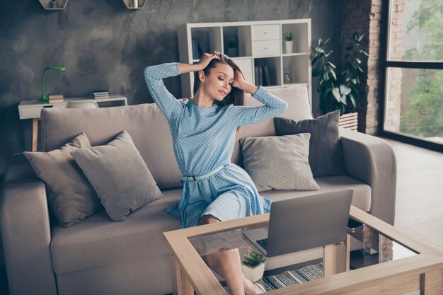 Photo of attractive beauty lady look notebook online video call\
internet meeting private chat photographing set blogger quarantine\
stay home sit couch wear blue dress living room indoors