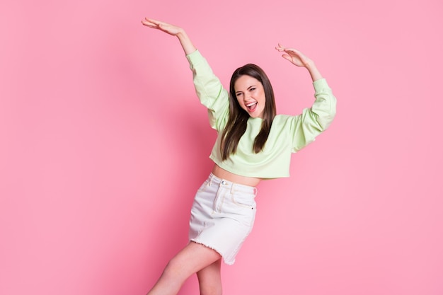 Фотография привлекательного фанк-юноши-миллениала, дама поднимает руки, танцует, студенты, вечеринка, стройная фигура, носит повседневный зеленый пуловер, голый живот, джинсовая юбка, изолированный розовый цвет фона