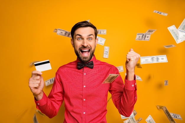 Photo of attractive funny guy hold plastic credit card rich person money bucks falling everywhere screaming wear trendy red shirt bow tie clothes 