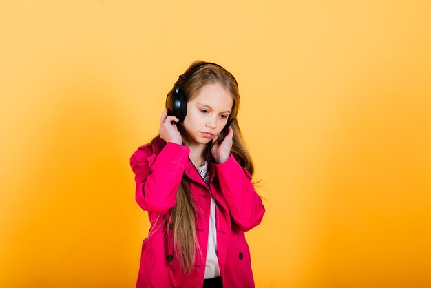 Photo of attractive girl using wireless headphones isolated over yellow background, studio