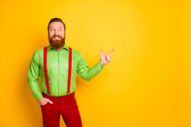 Photo of attractive hipster guy indicate finger empty space presenting black friday shopping season opening wear green shirt red suspenders pants isolated bright color