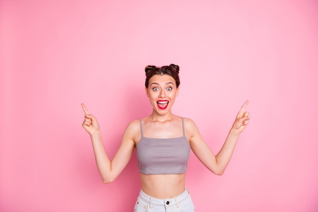 Photo of attractive lady cute buns red lips slim shapes indicate both arms empty space show low prices offer wear casual grey short top naked belly isolated pink color