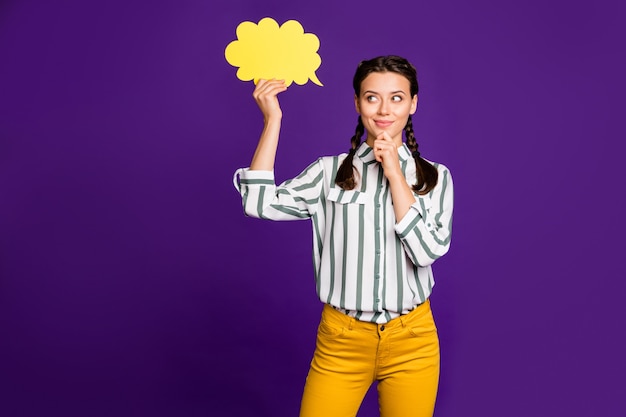 Photo of attractive lady hold paper mind cloud think over creative dialogue answer hand on chin wear striped shirt yellow trousers isolated purple color background