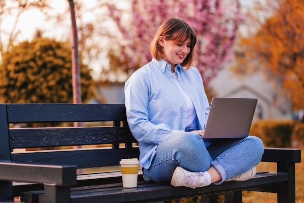 Photo of attractive lady student sit on bench in green park browsing notebook chatting do home tasks