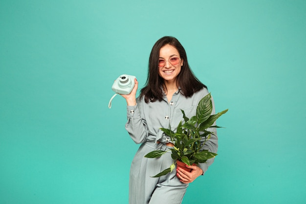 Photo of attractive lady in sunglasses holds camera, plant and has some fun