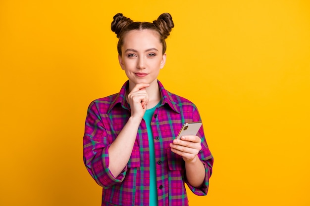 Photo of attractive minded teen lady hold telephone hands blogger think of writing creative post arm on chin wear casual plaid magenta shirt isolated yellow bright color background