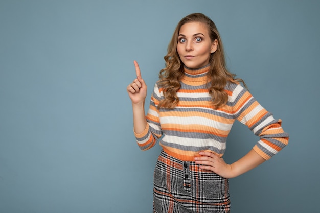 Photo of attractive positive young woman pointing finger up at copyspace presenting ads promo with wow omg sincere emotions wearing good look outfit isolated over wall with free space.