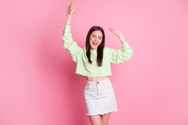 Photo of attractive pretty lady raise arms dancing disco party slim figure excited dancer wear casual green crop pullover naked belly jeans short skirt isolated pink pastel color background