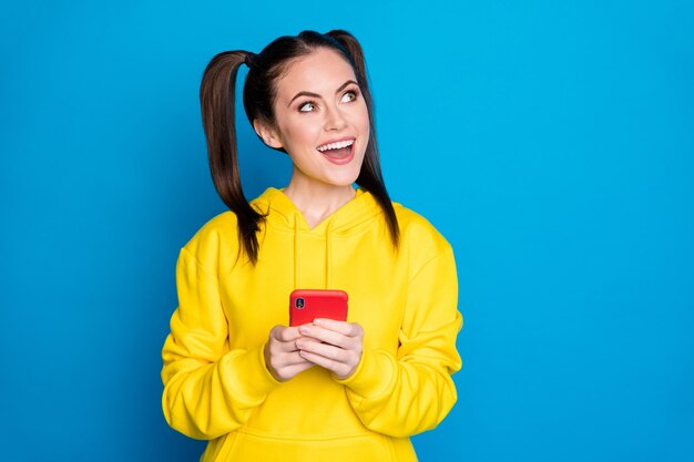 Photo of attractive pretty lady two tails hold telephone look up empty space think over new creative post blog wear casual yellow hoodie pullover isolated bright blue color background