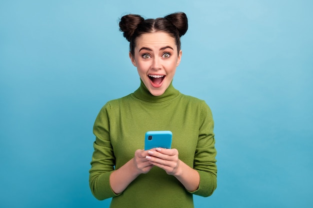 Photo of attractive pretty teen lady open mouth browsing telephone read blog post comments check followers subscribers wear green turtleneck isolated blue color wall