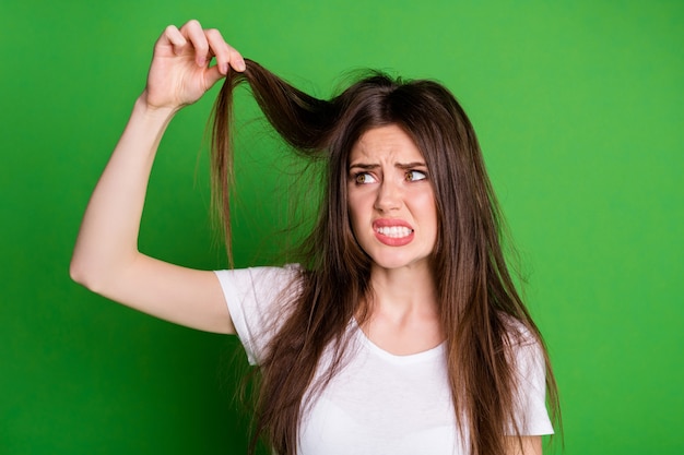 Foto foto di una donna attraente e triste che indossa una maglietta bianca che tiene i capelli con le estremità asciutte sullo sfondo di colore verde isolato