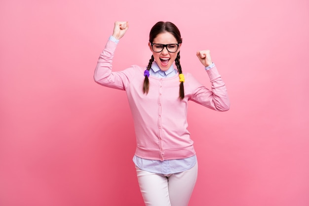 Photo of attractive student lady good mood self-confident person raise fists screaming celebrate money win wear shirt pullover specs trousers isolated pastel pink color background