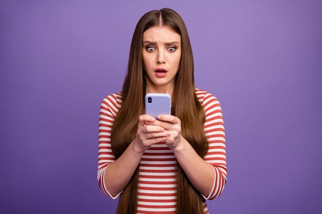 Photo of attractive terrified lady look open mouth telephone screen read negative comments blog post frightened wear casual striped shirt isolated pastel purple color wall