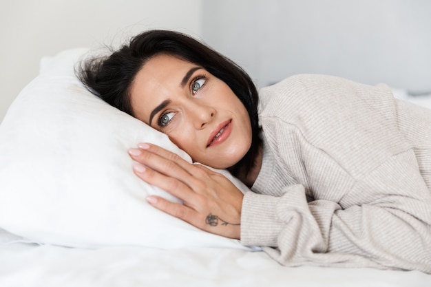 Photo of attractive woman 30s lying in bed, on white pillow at home