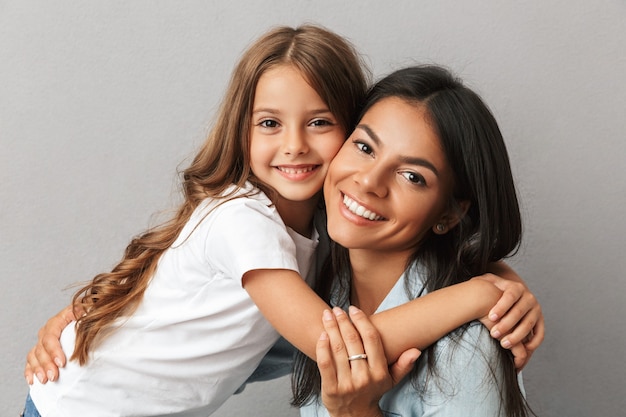 Photo of attractive woman with little daughter smiling and hugging together, isolated over gray