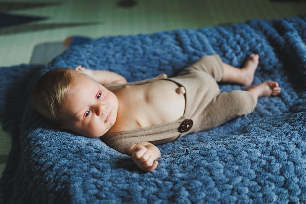 Photo of a baby in a knitted overall A small newborn boy lies on a gray knitted blanket Portrait of a onemonthold baby