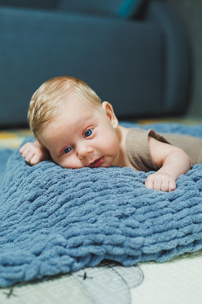 編み物のオーバーオールを着た赤ちゃんの写真新生児の男の子が灰色の編み物毛布の上に横たわっている1ヶ月の赤ちゃんの肖像画