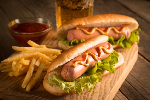 Photo of barbecue grilled hot dog with yellow mustard and ketchup on wooden background. Hot dog sandwich with potato fries and sauces.