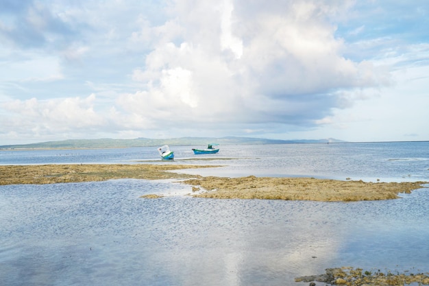 A photo of a beach with boats in the water and the sky is blue and white.