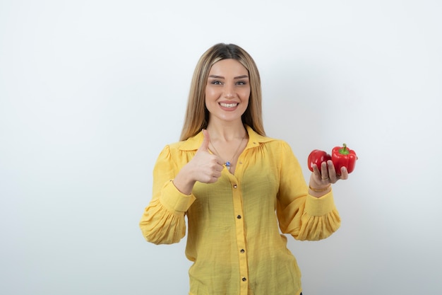 Photo of beautiful blonde woman holding red bell peppers and giving thumbs down