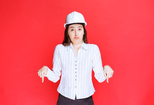 Photo of a beautiful business woman wearing safety hat pointing down with fingers.