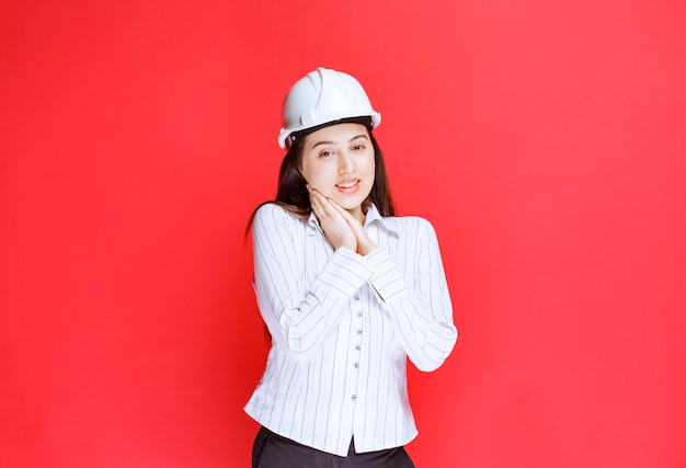 Photo of a beautiful business woman wearing safety hat standing against red wall.