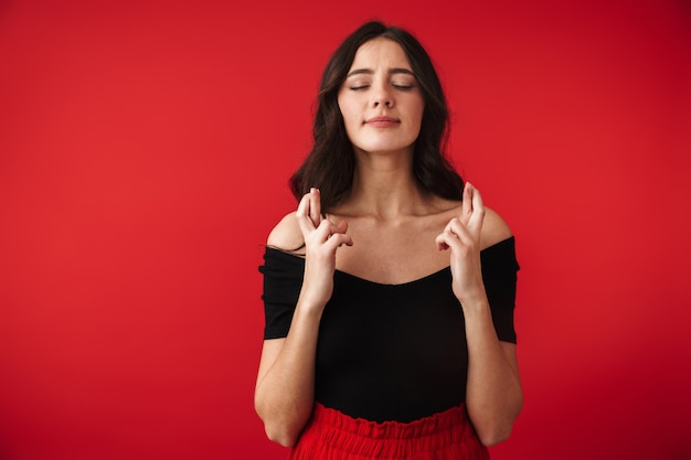 Photo of a beautiful cute young woman standing isolated over red wall make please hopeful gesture.