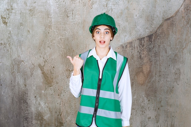 Photo of beautiful female architect in green helmet pointing