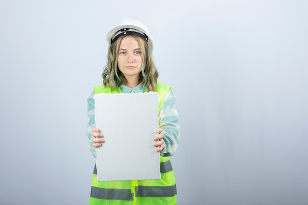 Photo of beautiful female engineer holding empty canvas over white wall. High quality photo