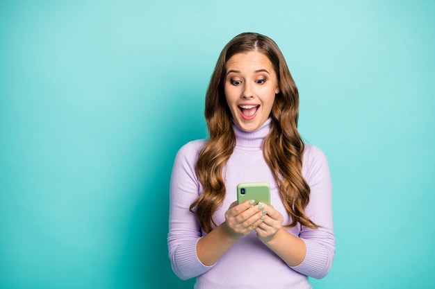 Photo of beautiful funny lady hold telephone hands reading blog post positive comments overjoyed wear purple violet turtleneck isolated teal blue pastel color
