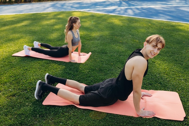 Photo of a beautiful happy couple in sportswear performing stretching exercises on a yoga mat