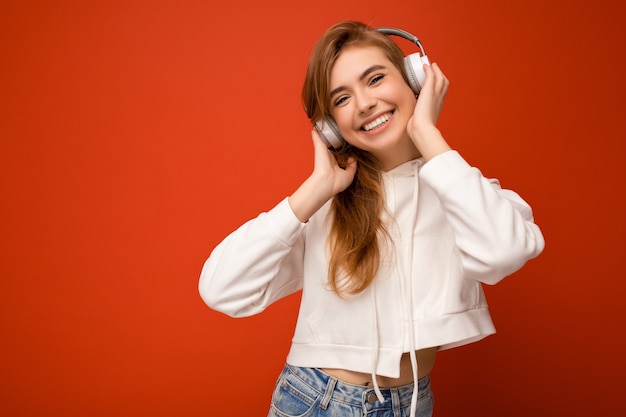 Foto di bella giovane donna bionda sorridente felice che porta la felpa con cappuccio bianca isolata sopra variopinta