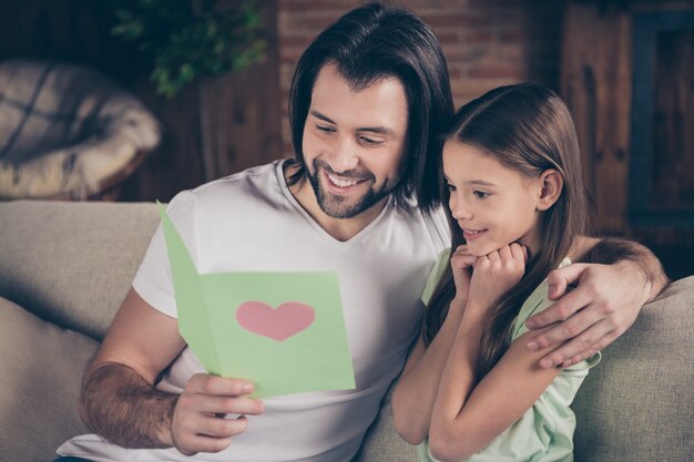 Photo of beautiful little adorable girl and handsome young daddy sit on comfy sofa