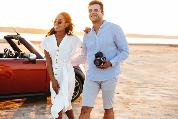 아름다운 다민족 커플 남녀가 함께 껴안고 야외에서 자동차로 복고풍 카메라와 함께 걷는 사진